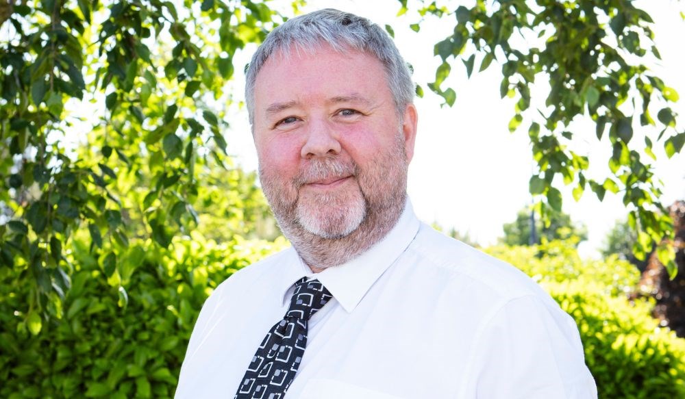 Headshot of man stood outside wearing white shirt and dark tie